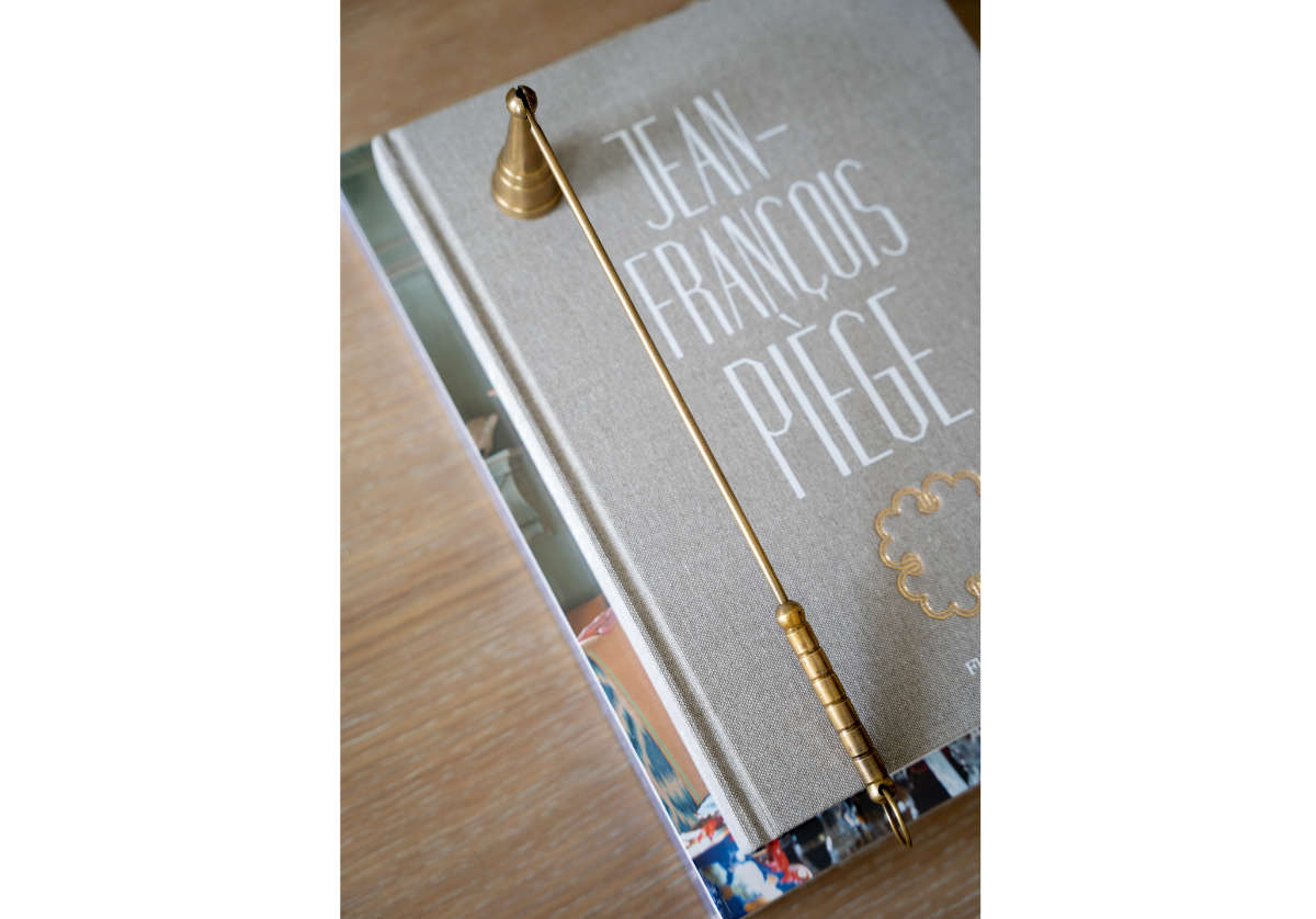 Brass antique candle snuffer pictured on top of a gray book.