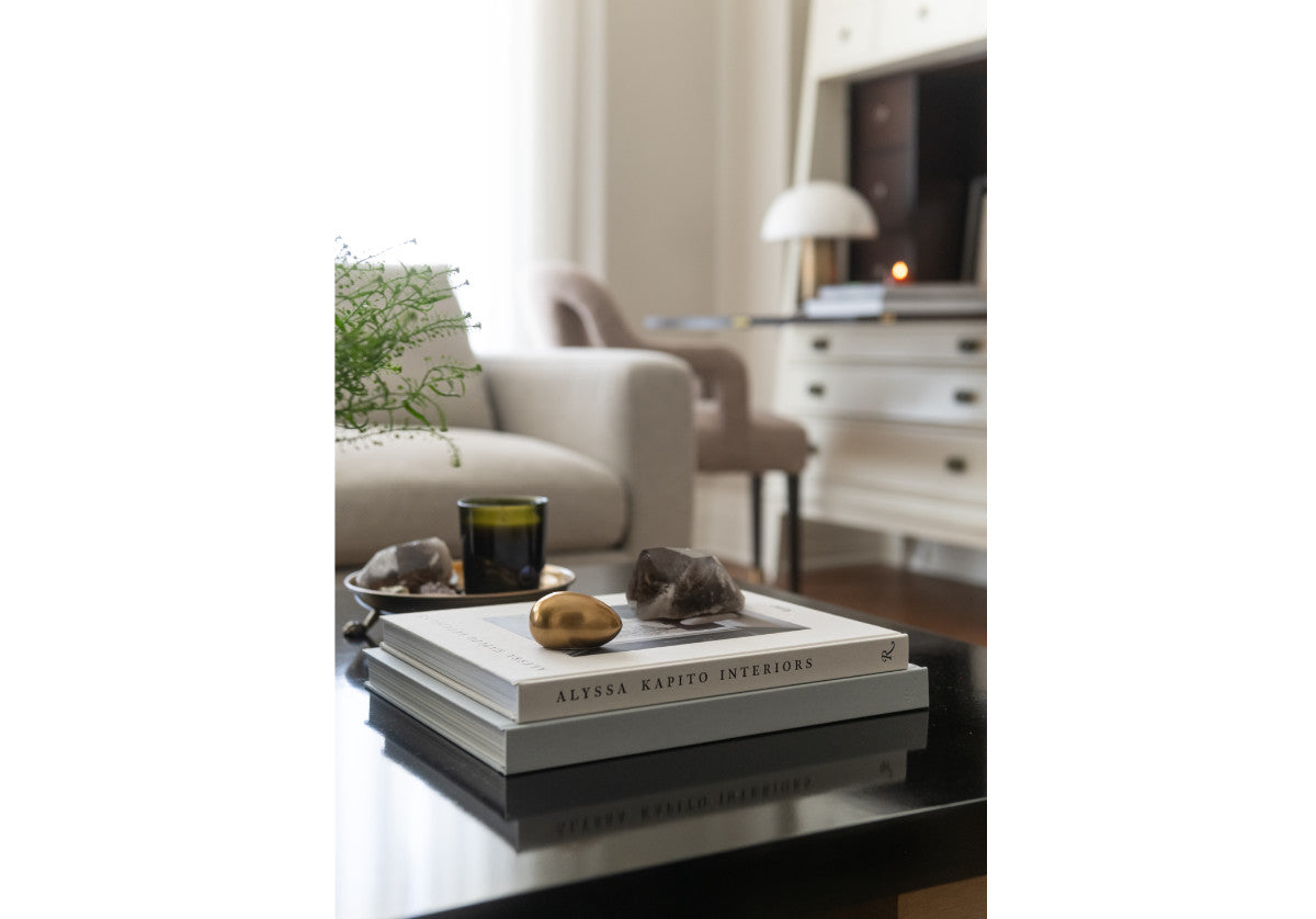lifestyle photo of brass egg on a pile of books in a living room.
