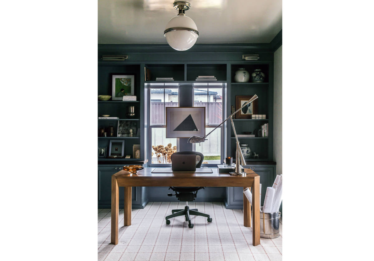 The Brooklyn Desk showcases a beautiful bleached walnut finish set on a walnut composite base. Its clean-lined from is subtly contrasted by angled drawers with petite bronze knobs for added dimension and sophistication. Easily style at the foot of a bed or in an office for an eye-catching design.
we can see the brooklyn in the center of a matte blue office with a laptop and desk lamp.