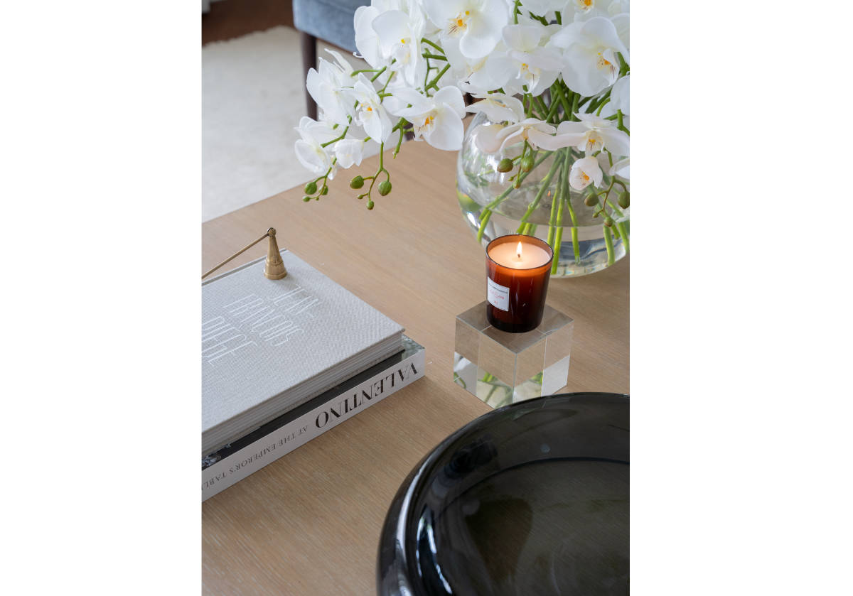 lifestyle photo of the large crystal cube with a lit candle on top of it with books to the left and a candle snuffer.
