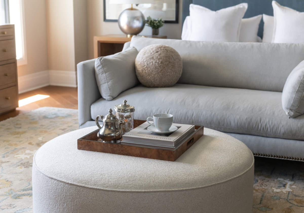 lifestyle shot of the burled wood tray with a teapot inside of it on top of the piper ottoman.
