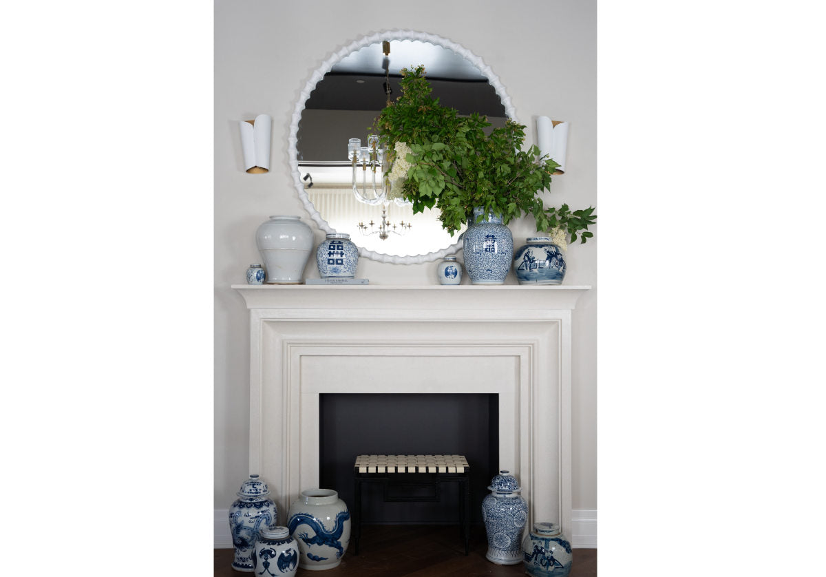 lifestyle photo of astrid sconce next to a decorative mirror. placed above a series of blue and white jars on fireplace mantle.
