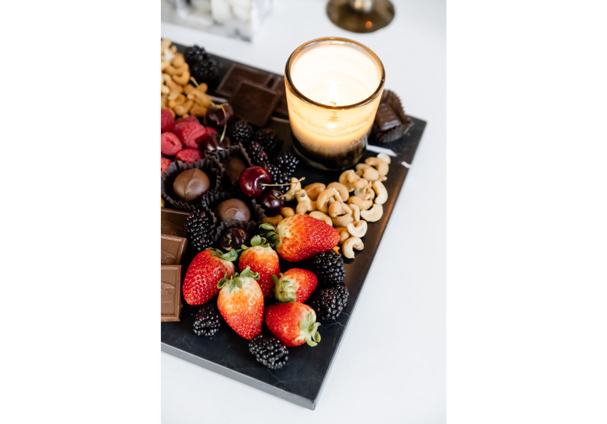 large black marble cutting board shown with fruits and chocolates on it.