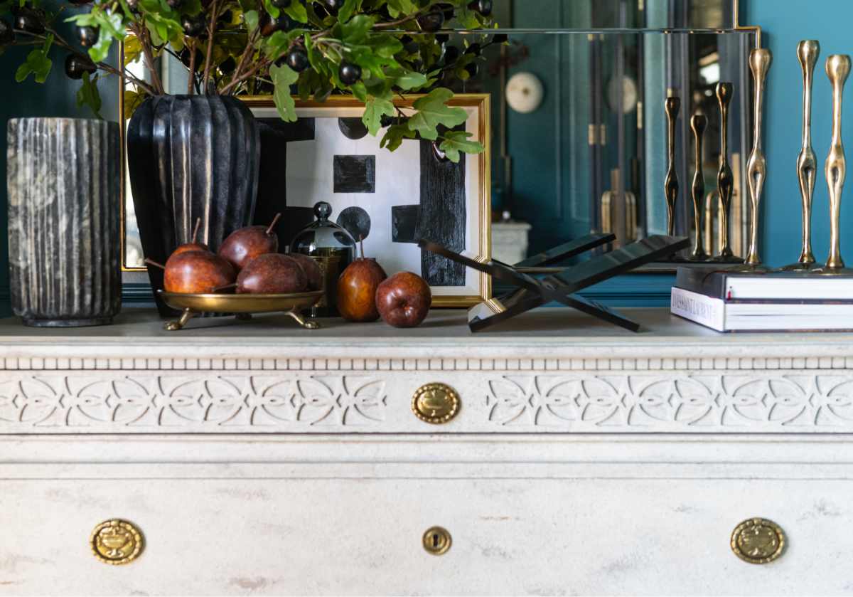 large clawfoot dish on top of a white dress with gold hardware. the tray is sitting next to a lucite book display and candle sticks.