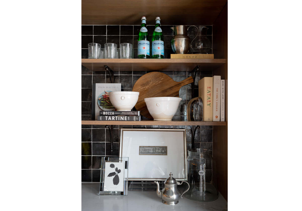 crystal frame with silver teapot and floating shelves holding other decorative items such as wood cutting board and crystal bookends and cook books.