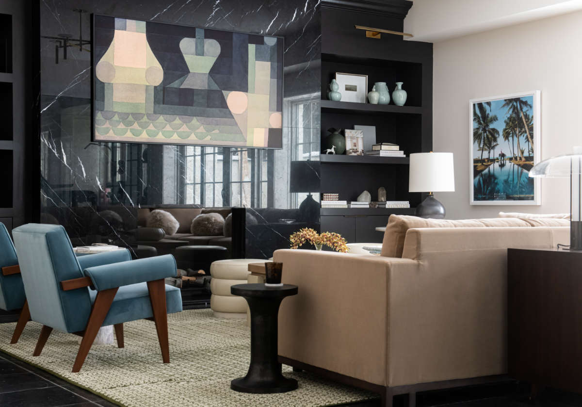 lifestyle photo of a living room. there is a tan couch and blue chairs. on the black shelving there a blue vases, books, and other decor including the brass horse.