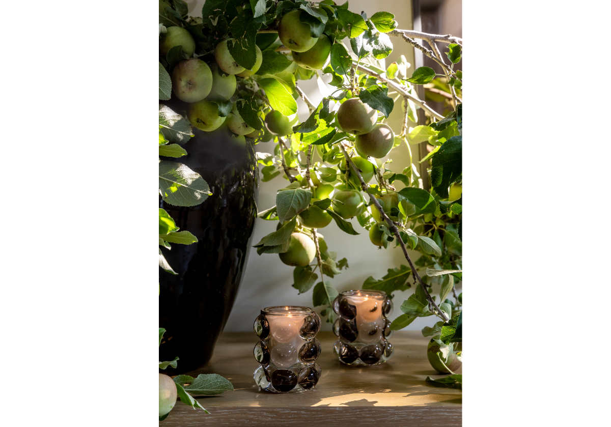 close up of large black vase with apple stems sticking out of it on a table.