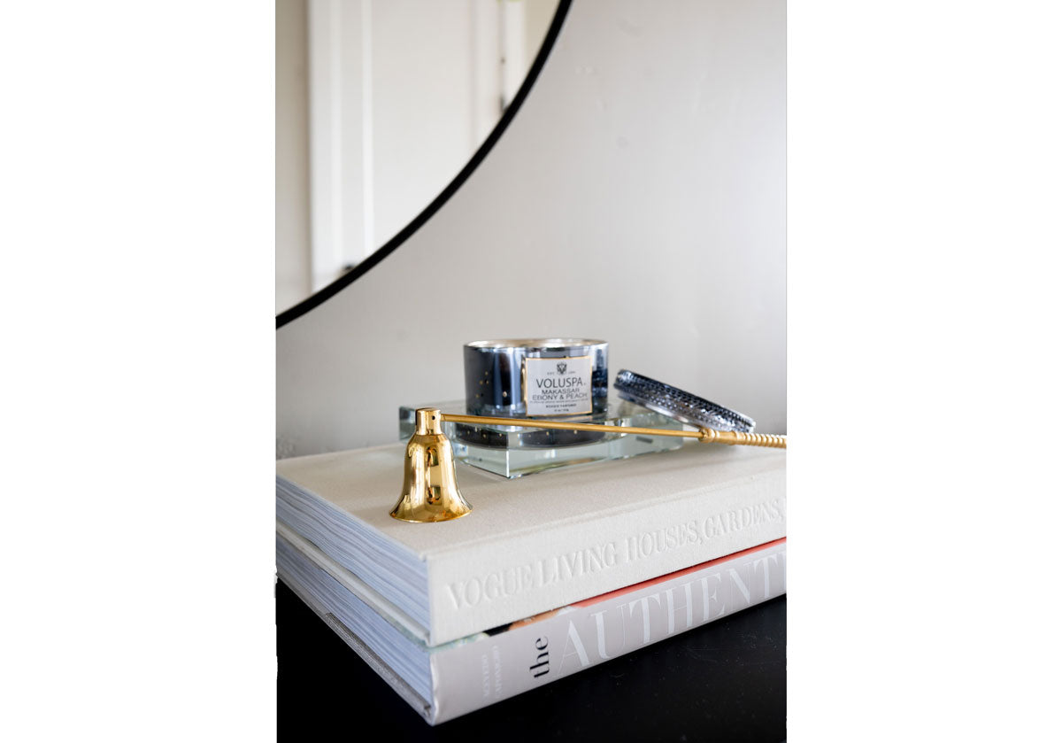 brass candle snuffer on top of books with a candle.