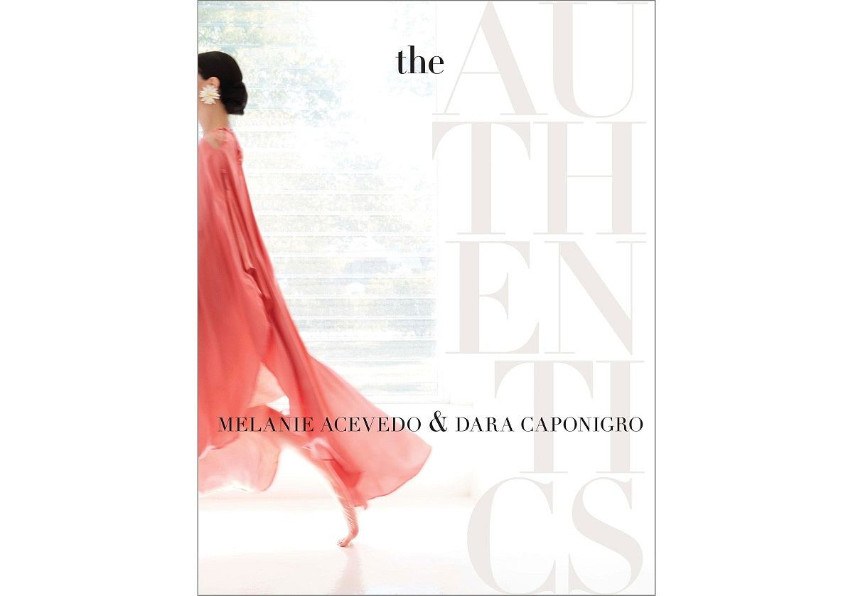 A woman in a flowing pink dress walks gracefully by a large window, the soft light creating an airy atmosphere that exemplifies true style. THE AUTHENTICS by Random House Inc, photographed by Melanie Acevedo & Dara Caponigro, celebrates tastemakers of elegance on the right side.