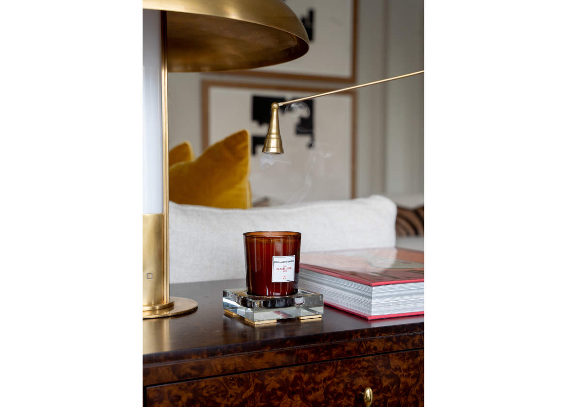 Someone off camera is holding the brass antique candle snuffer over a candle on top of a dresser. 