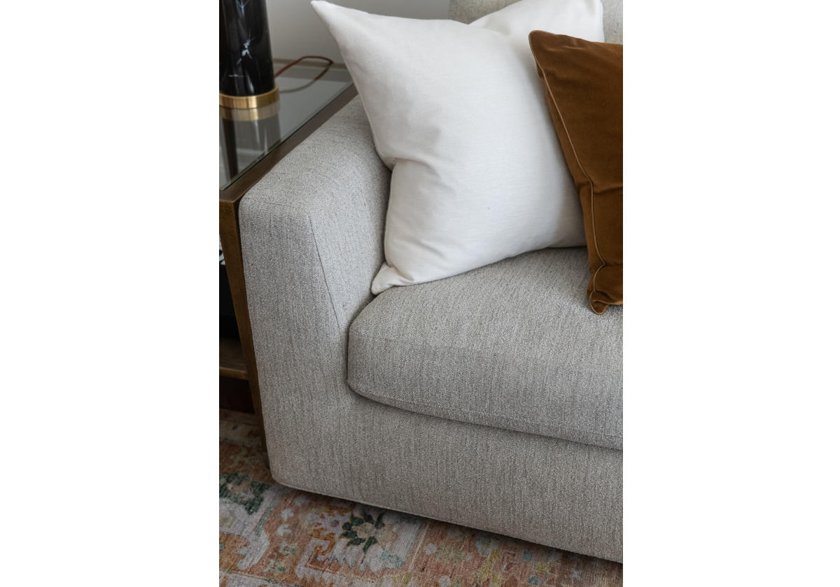 the august sofa seen with pillows. The angled arms and walnut-stained plinth base add dimension and interest making this piece beautifully suited for spacious living or family rooms. Its neutral woven fabric is subtly accented with a blue loop undertone for added depth