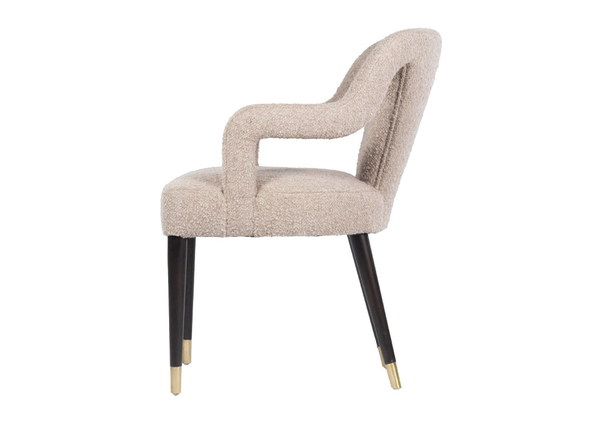 side view of the Bobbie showcases a shapely form with its sloping back, curved arms, and canted legs. Covered in the industries finest Libeco fabric, created in Belgium, its Berber Linen upholstery in a versatile neutral elevates a sophisticated style. Brass-capped feet beautifully contrast its walnut-finished legs for a luxurious, tasteful design. facing to the left 