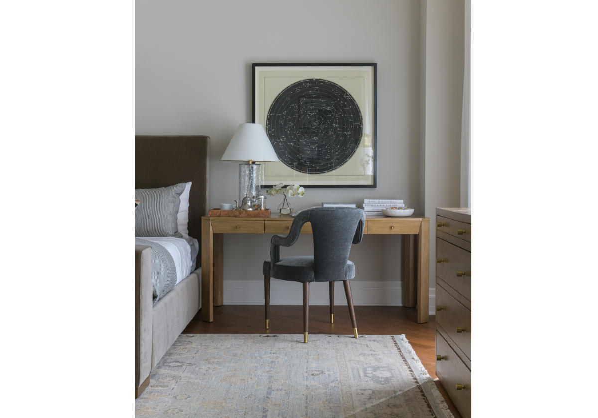 a lifestyle photo of the bobbie chair, sitting in front of the brooklyn desk next to a bed.  there is a lamp sitting on top of the desk. 