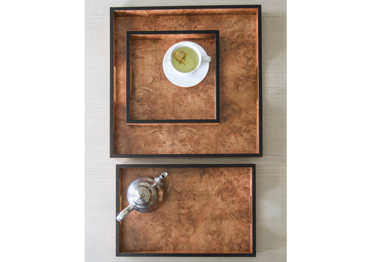 a lifestyle photo of each of the wood burled trays. the large and small square trays are inside of each other while the medium rectangle tray is alone with a teapot inside of it. 