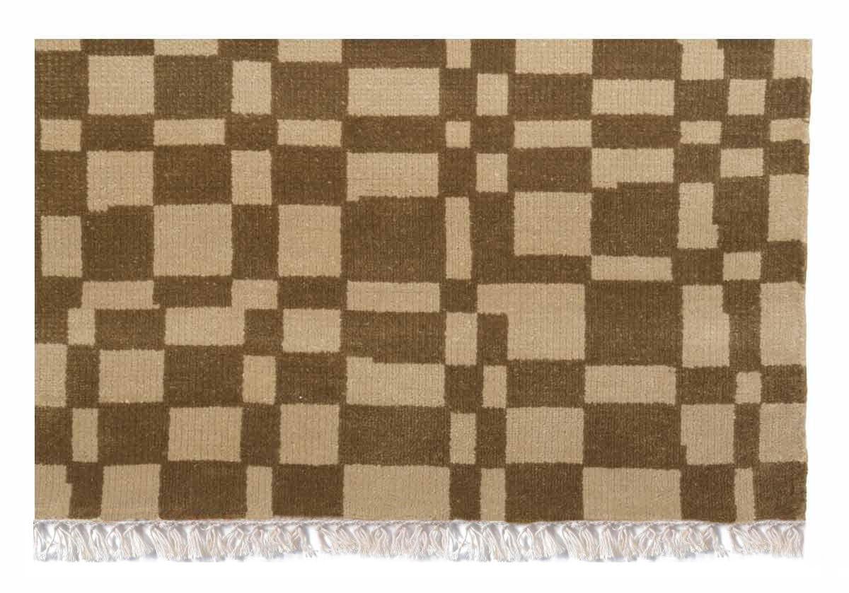 close up of corner of chess rug, with delicate white tassels at either end. taupe and light brown checkered pattern. 