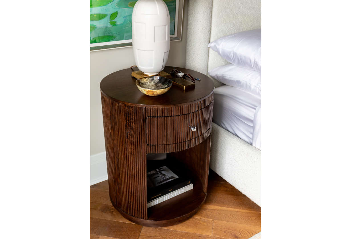 lifestyle photo of the cleo nightstand with a decorative lamp on top next to a bed. 