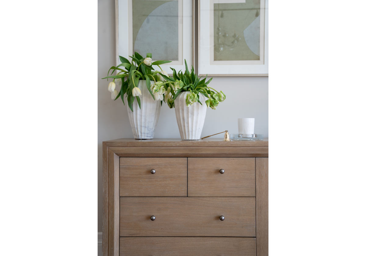 bell shaped brass candle snuffer on top of the theodore dresser next to white marble cases filled with lilies. 