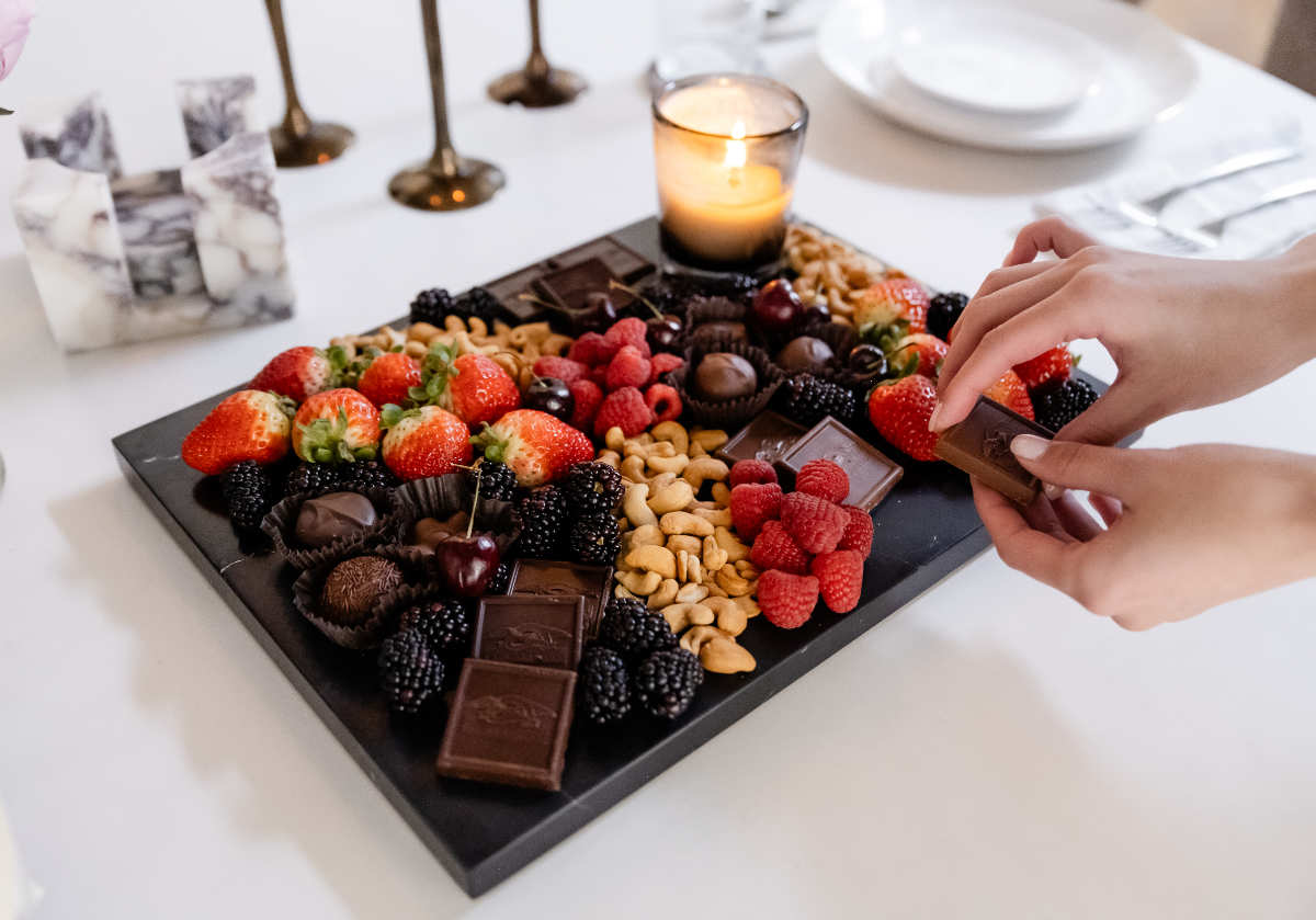 large black marble cutting board with chocolates and fruits on top with candle. 