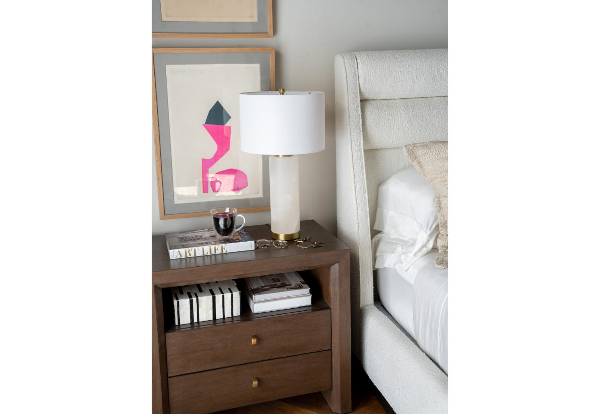 a photo of the blythe lamp a top the millie dresser. shown next to a bed in a bedroom with a piece of art behind it. 