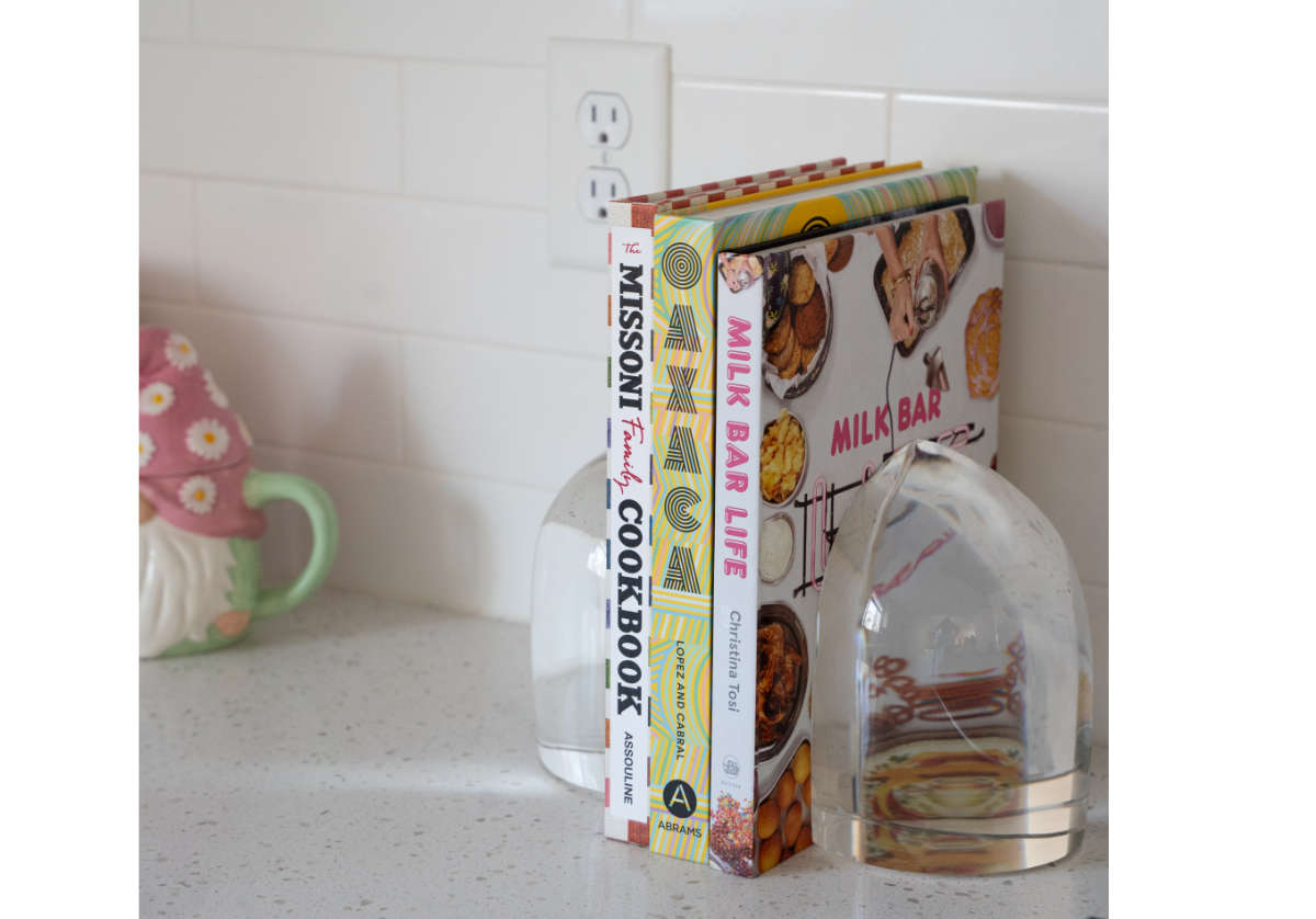 lifestyle photo of the crystal bookends holding up three different cookbooks in a kitchen on a counter. 