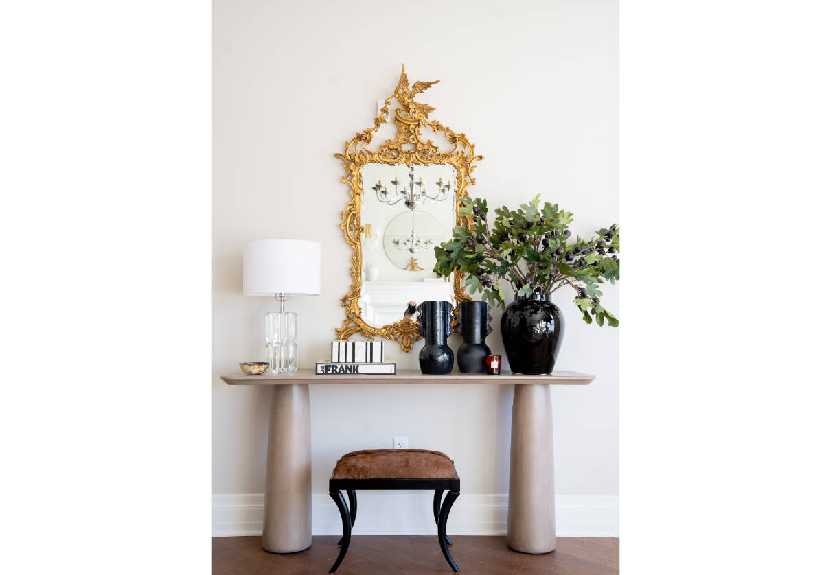 a photo pf the cate console holding books and large black vase with a mirror in the background hanging from the wall. 