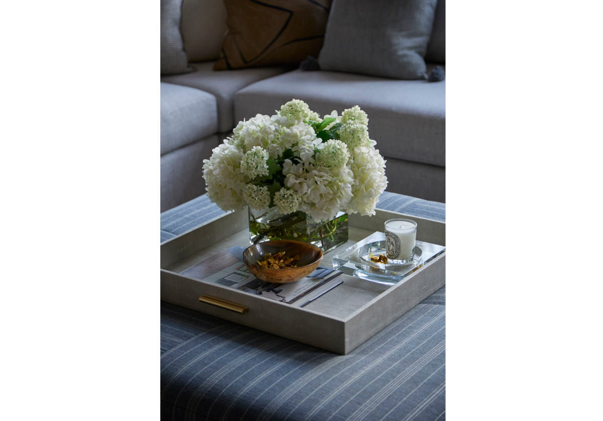 crystal candle dish seen inside of a decorative tray with flowers on top of ottoman. 