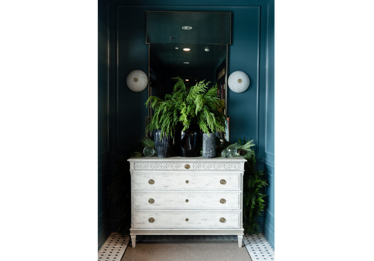 white distressed dresser with some marble vases and pine stems in them, crystal orb is on the left side of the dresser. 