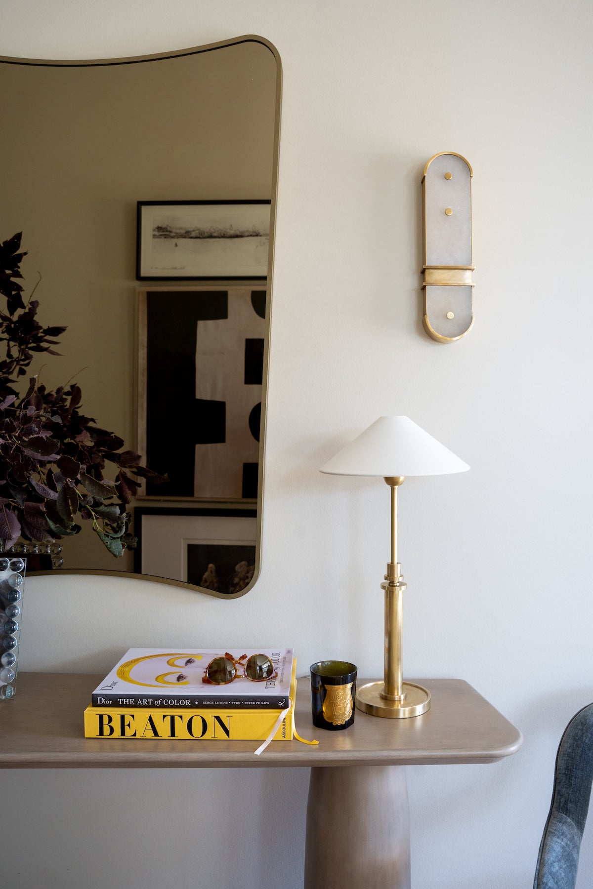 lifestyle shot of the domino sconce above a small table lamp on the cate console next to a mirror. 