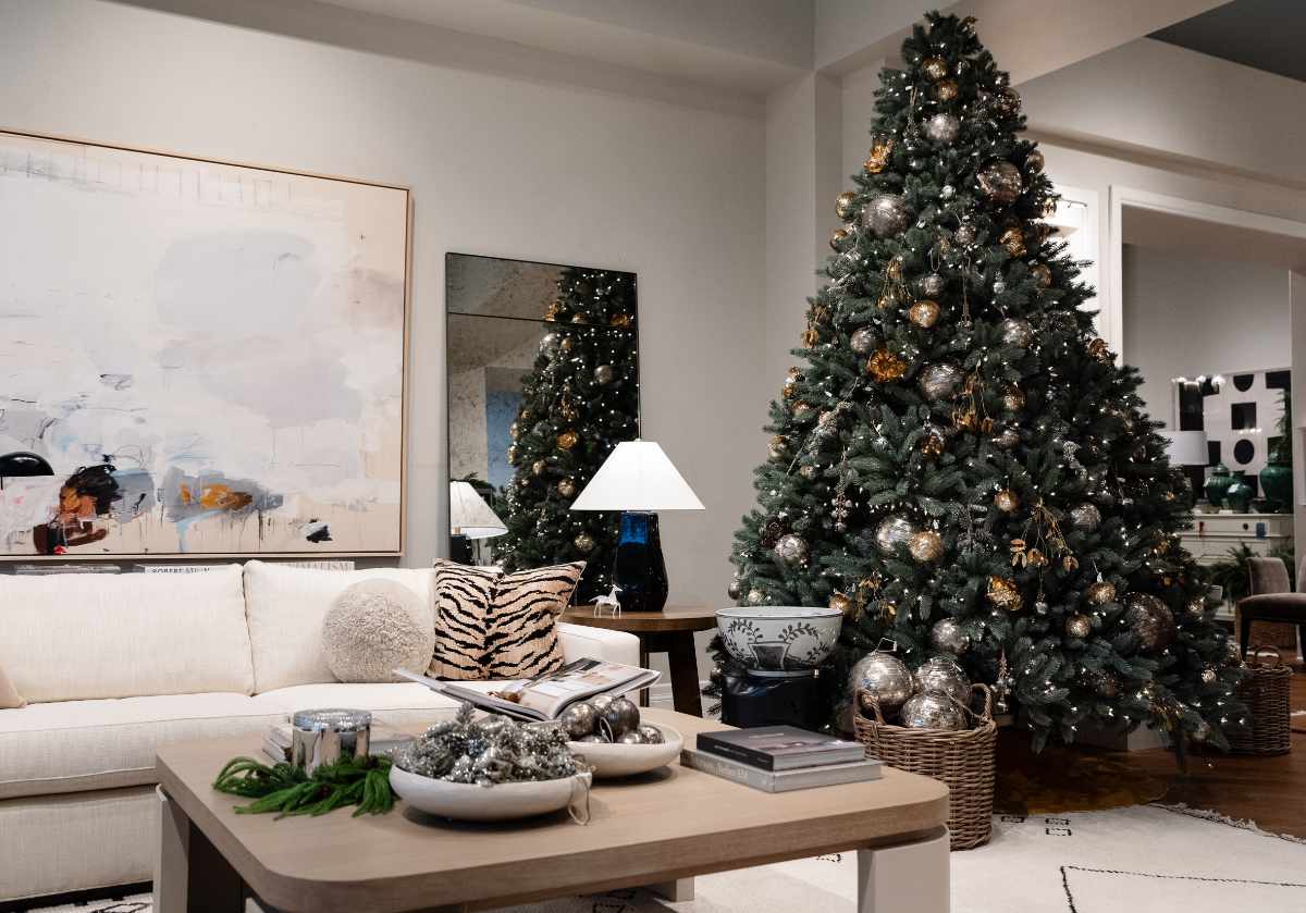 in a living room setting, the eden mirror can be seen leaning against a wall with a large sofa and tiger print pillows. with a coffee table and ornaments and a large christmas tree in the reflection of the eden mirror. 