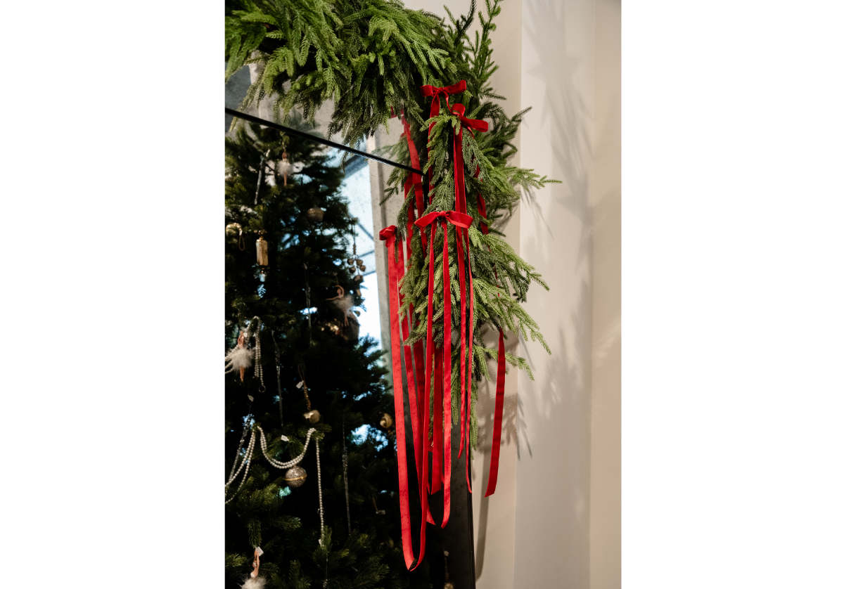 the eden mirror decorated with green garland and red ribbons stands beside a Christmas tree adorned with gold and white ornaments.