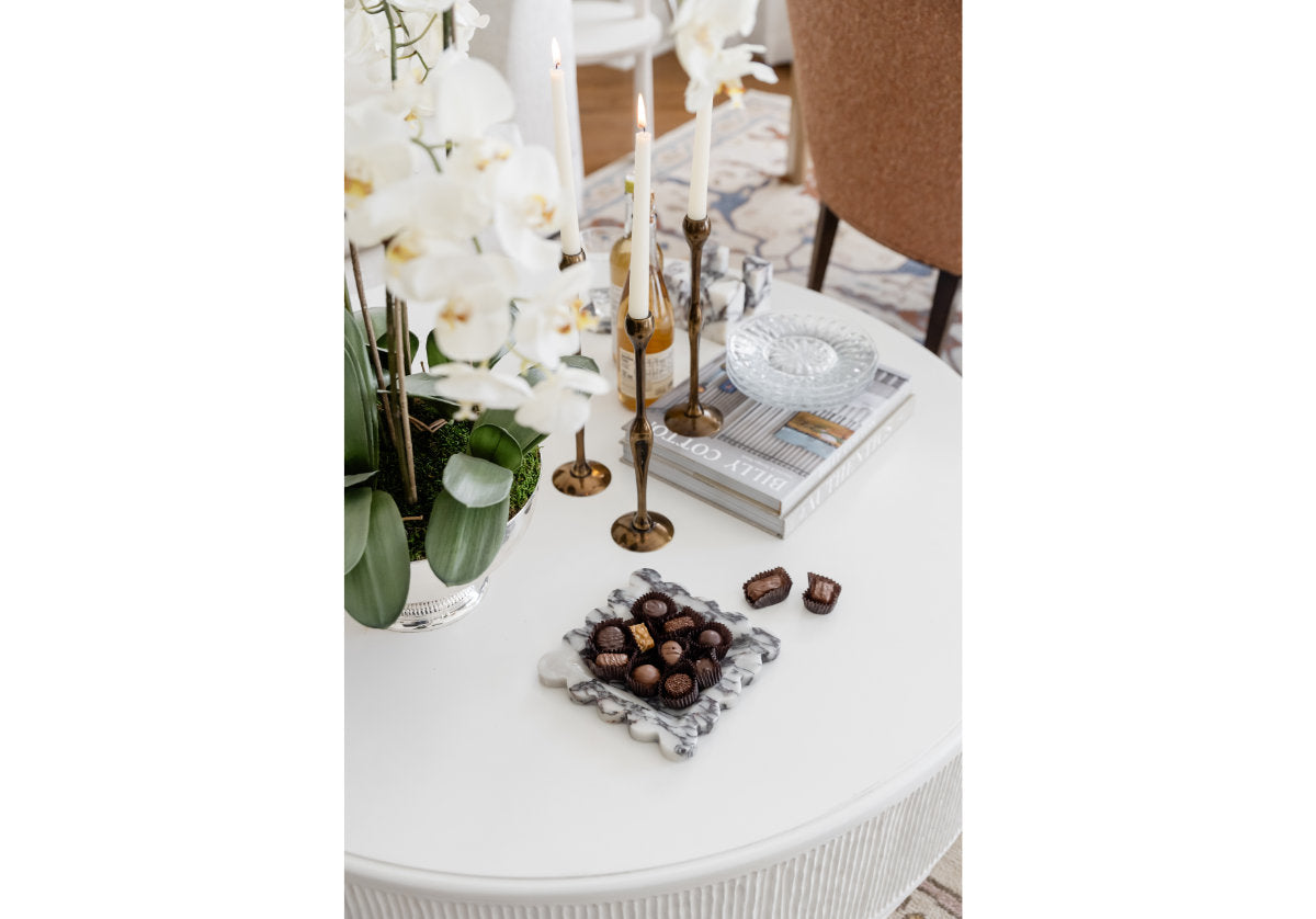 lifestyle shot of the figure brass candlestick on the lucca coffee table with the marble tray next to it. 