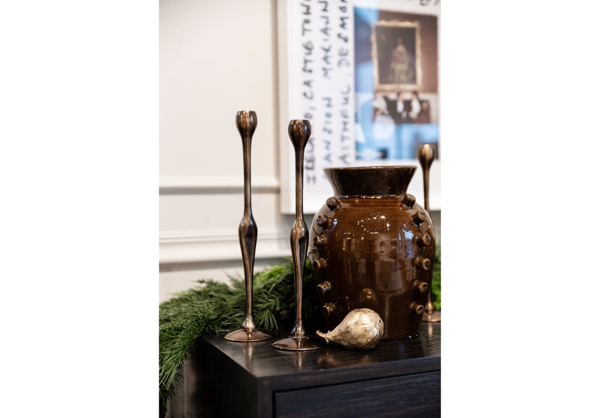 figure brass candlesticks next to a dark brown vase. 