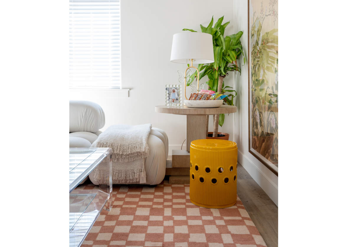 pink and white chess rug can be seen in a living room with a yellow garden stool and glass/crystal coffee table. 