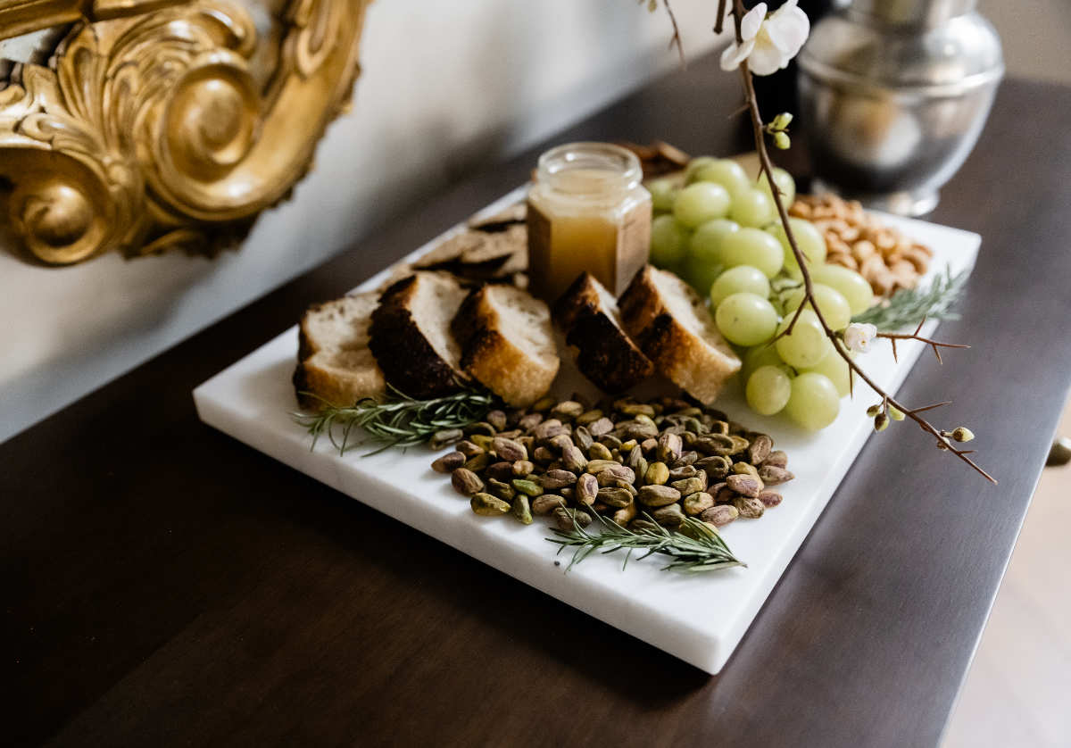 alice lane's large white marble cutting board seen with fruits and breads and nuts all over it, placed on a dresser. 