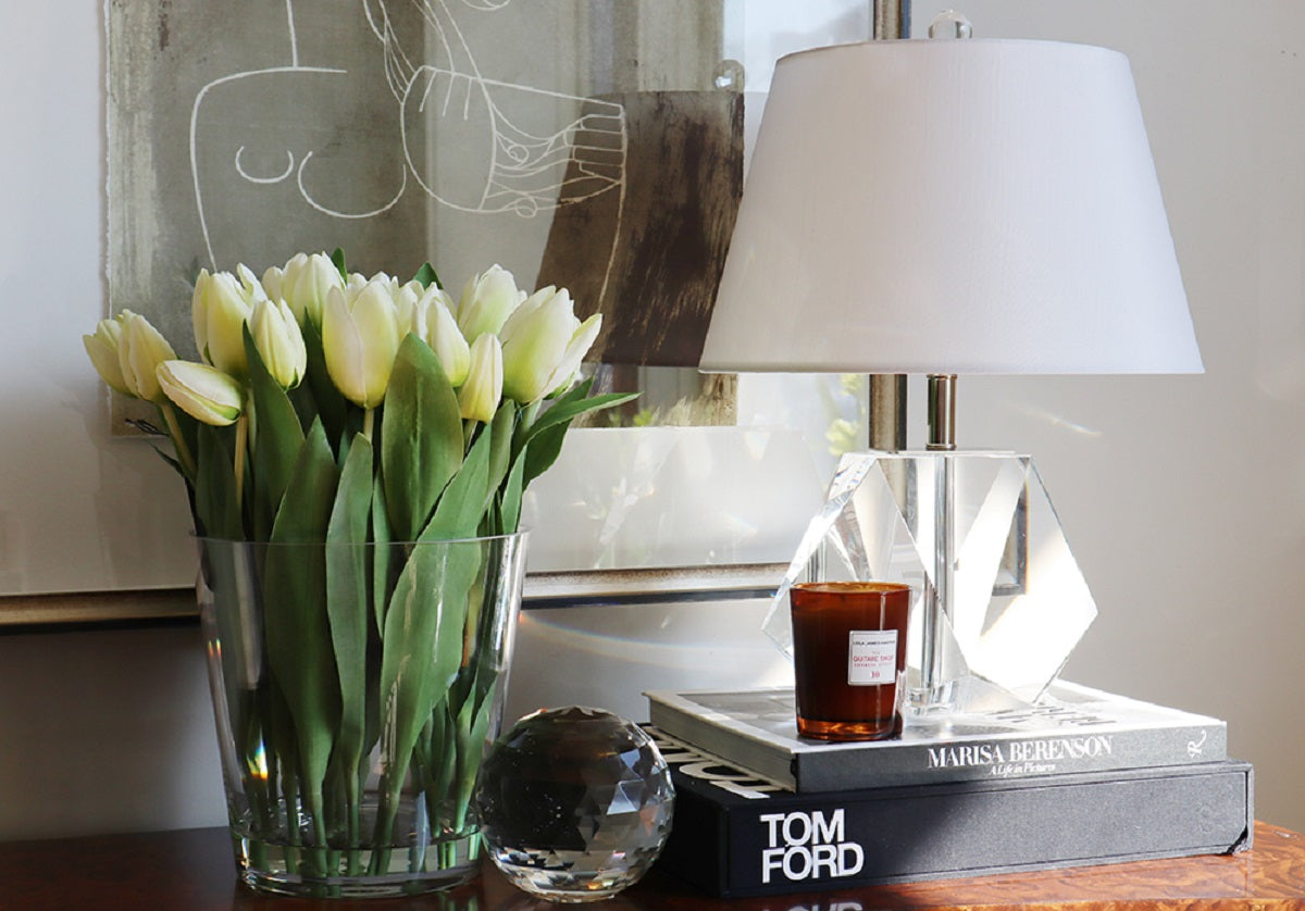 the birdie lamp can be seen on top of a pile of books next to a vase of tulips. 