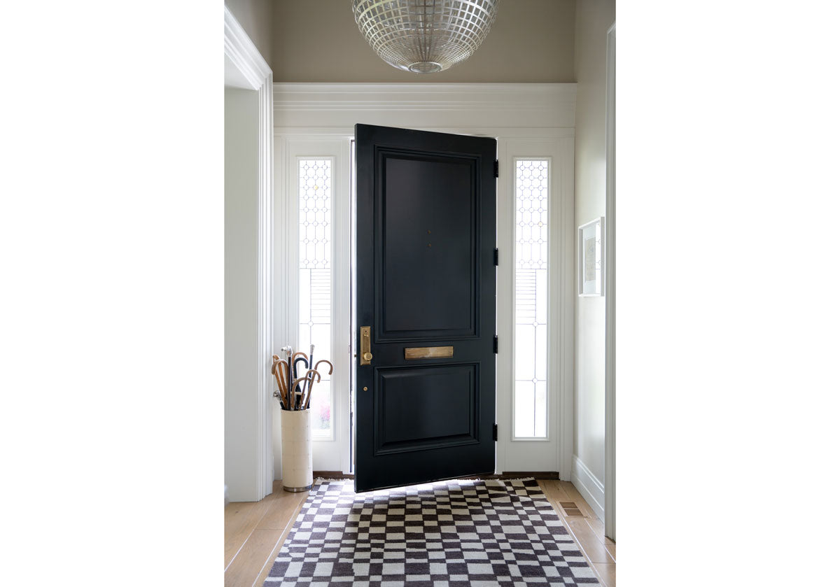 lifestyle photo of the chess rug in front of a black front door next to an umbrella holder. 