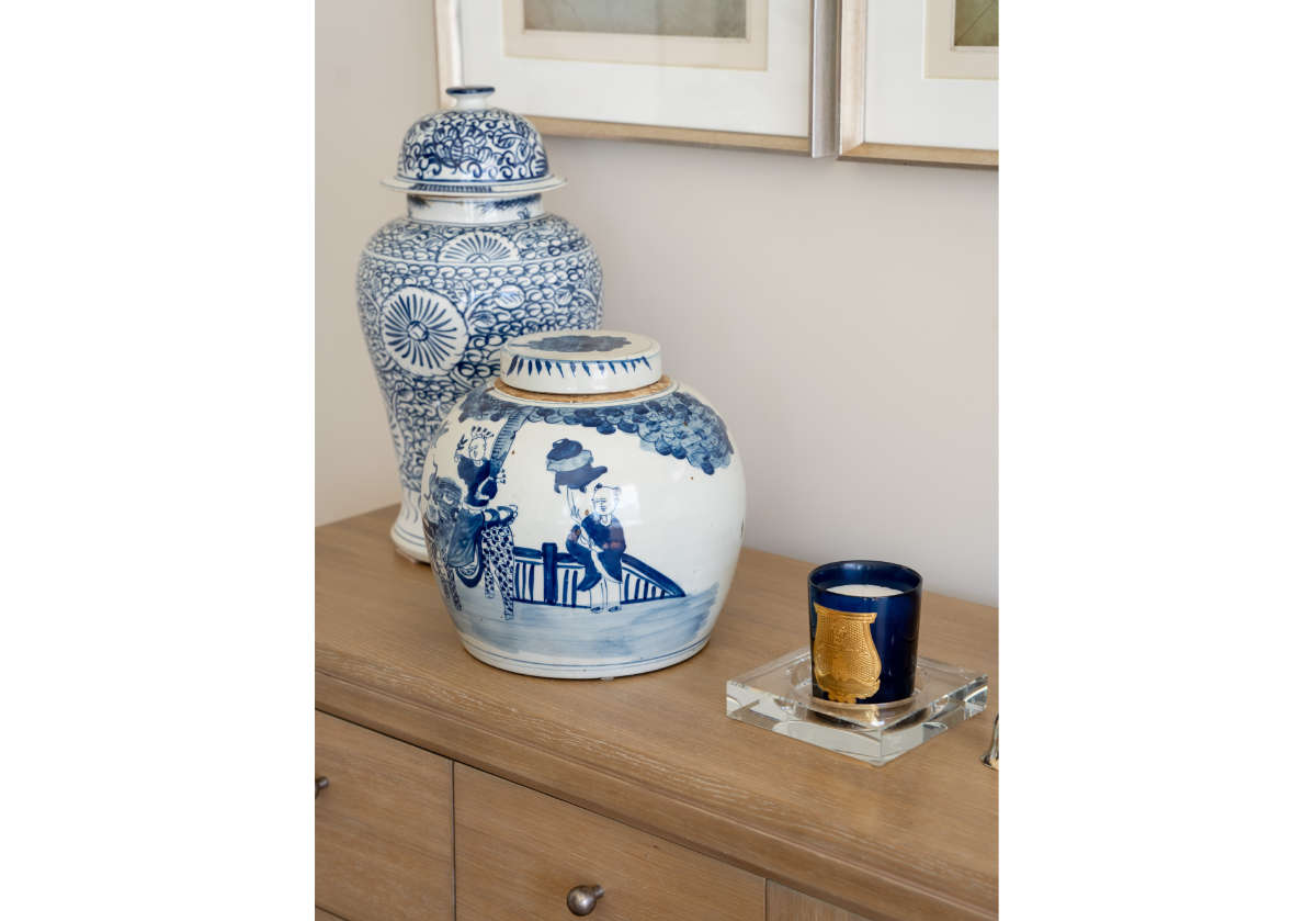 two large blue and white jars placed on top of a dresser with a crystal candle dish with a candle inside of it. 