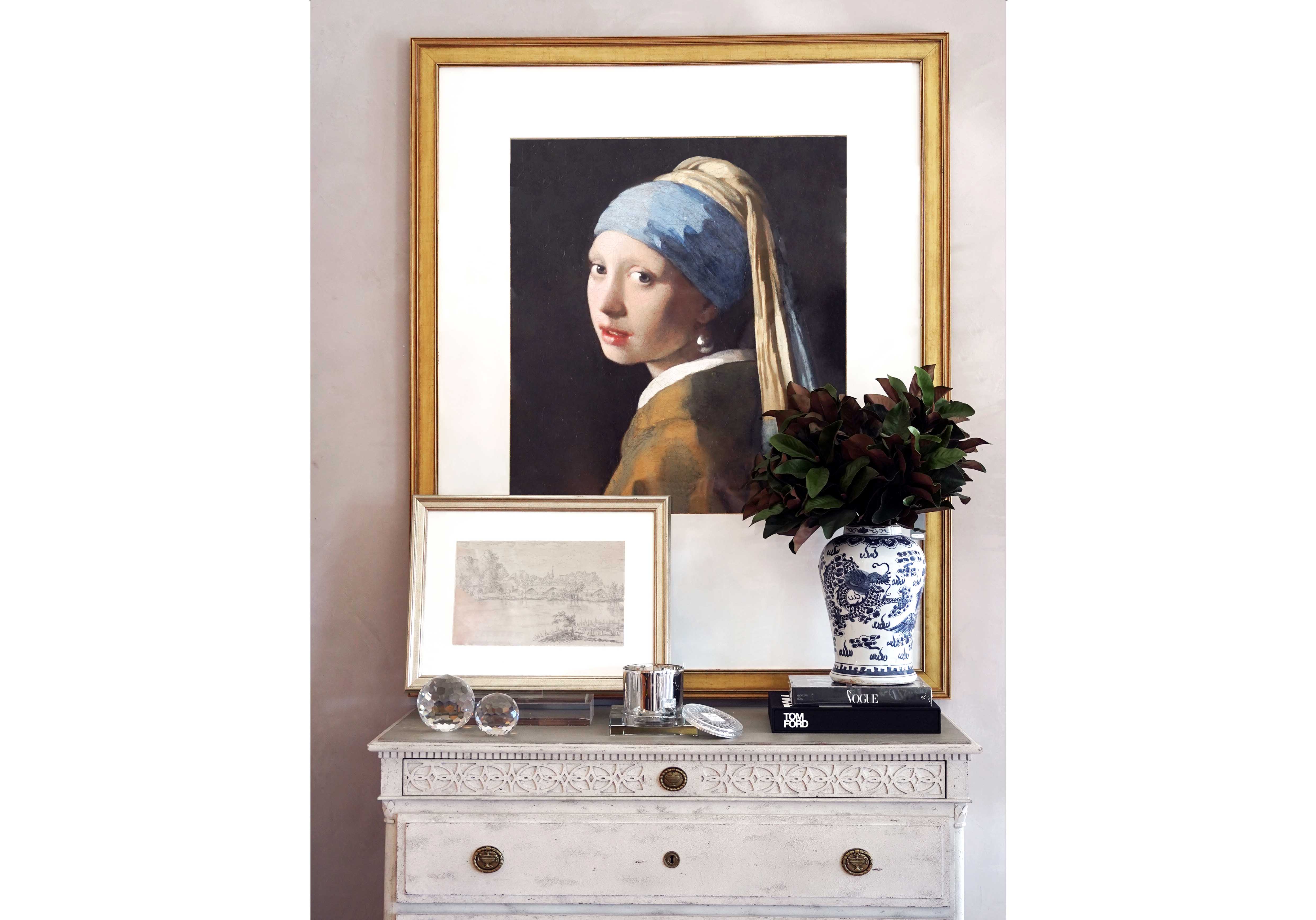 tom ford book with blue and white vase on it and crystal orbs on left side underneath and girl with the pearl earring on a white dresser. 