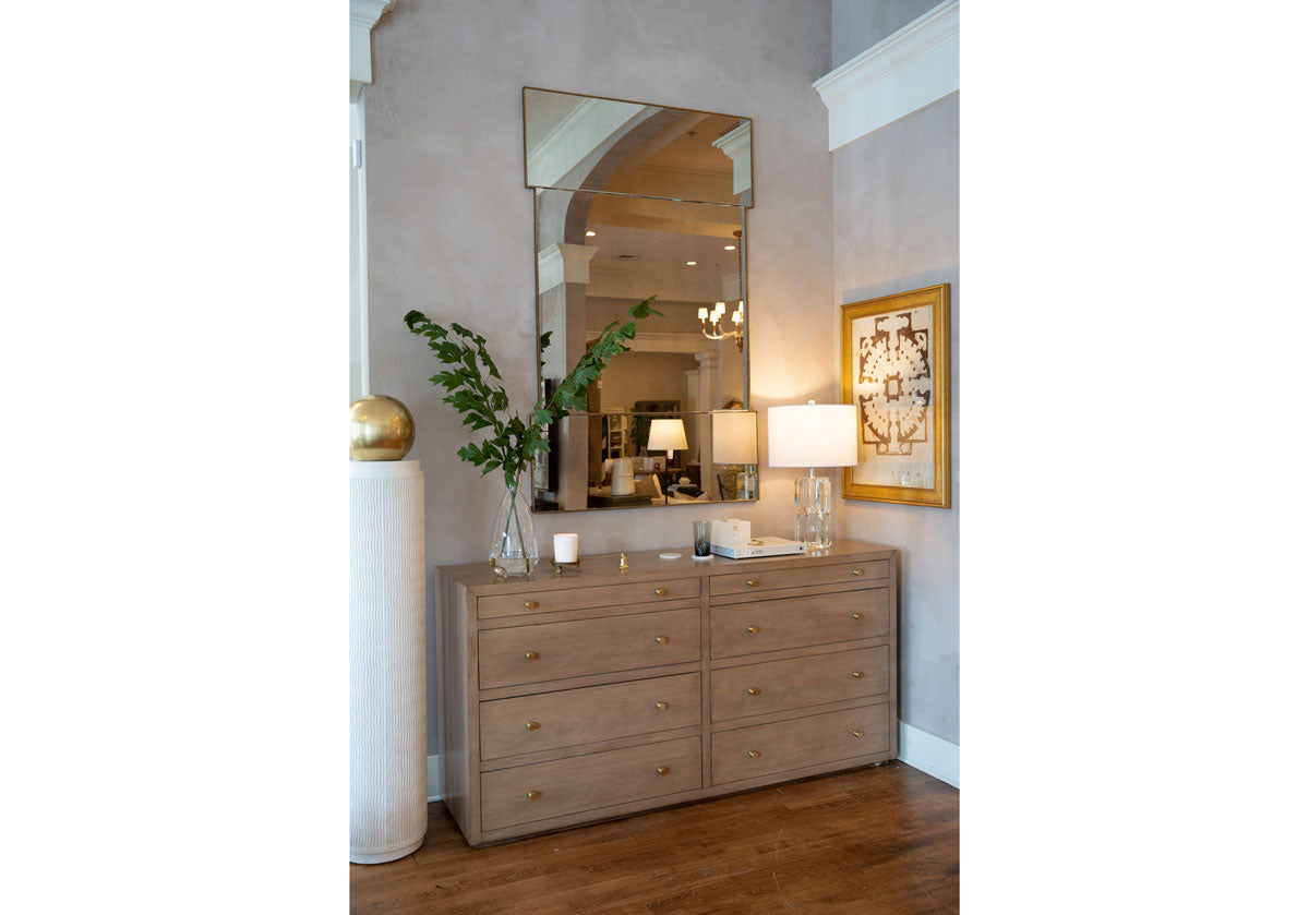 lifestyle photo of the brooklyn dresser with a large mirror above it and other decorative items. sitting next to a pedestal. 