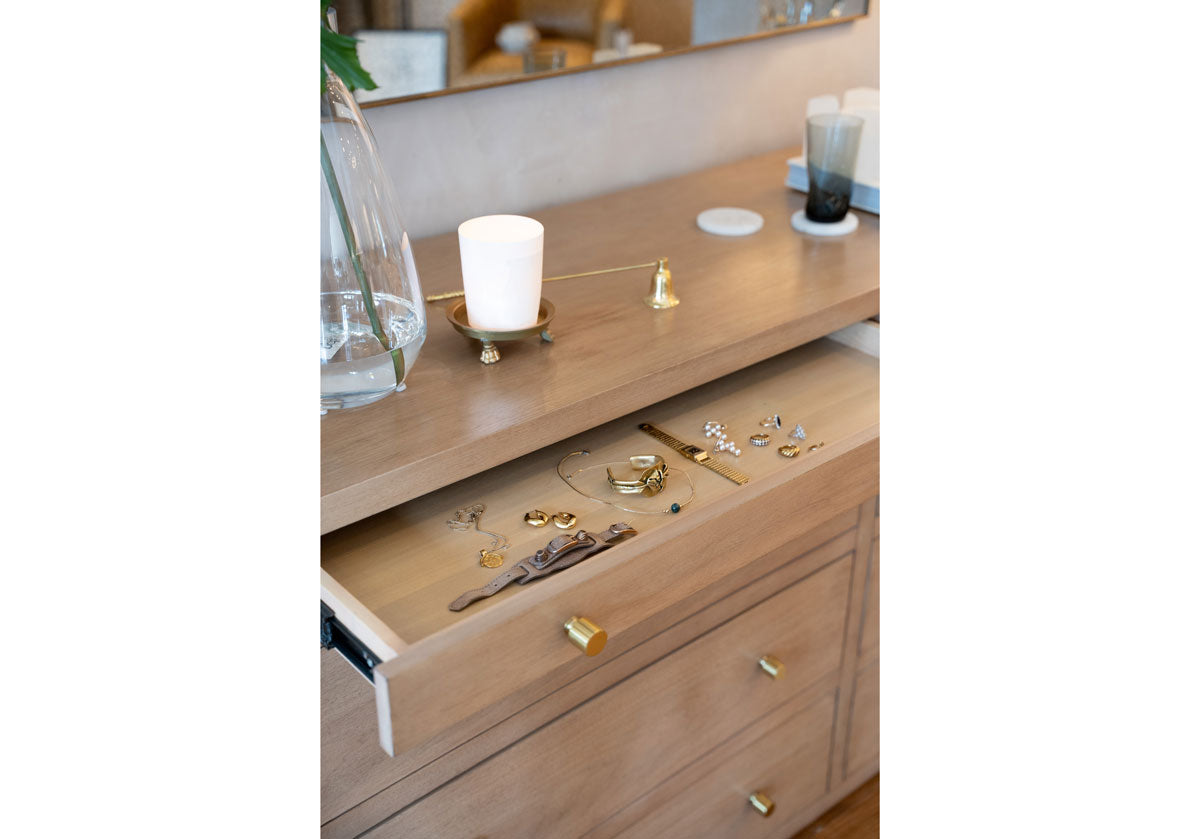 a close up of the brooklyn dresser with a drawer open and featured with jewelry inside. decorated with a brass clawfoot dish and brass candle snuffer. 