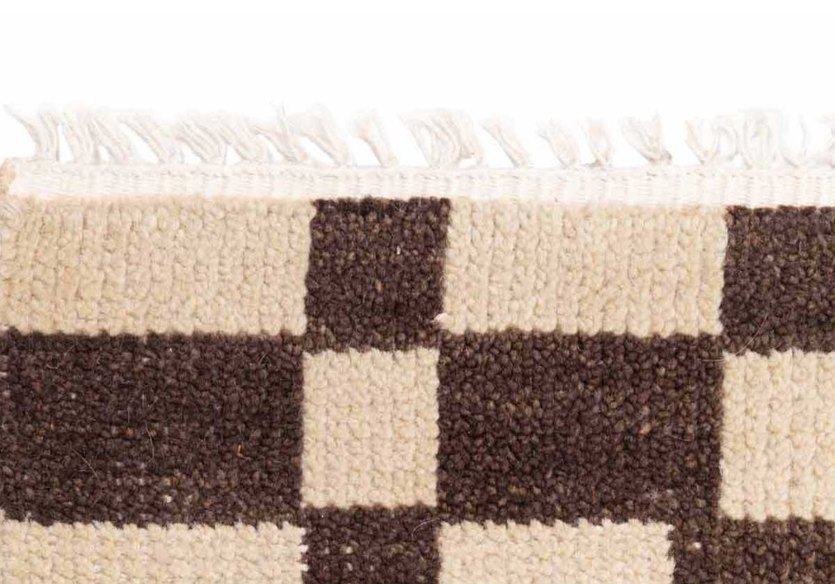 close up of the brown and white chess rug with white tassels on the end. 