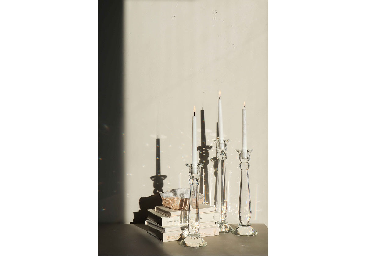 three crystal candle sticks in the sunlight, being shown with 3 books in the background. 