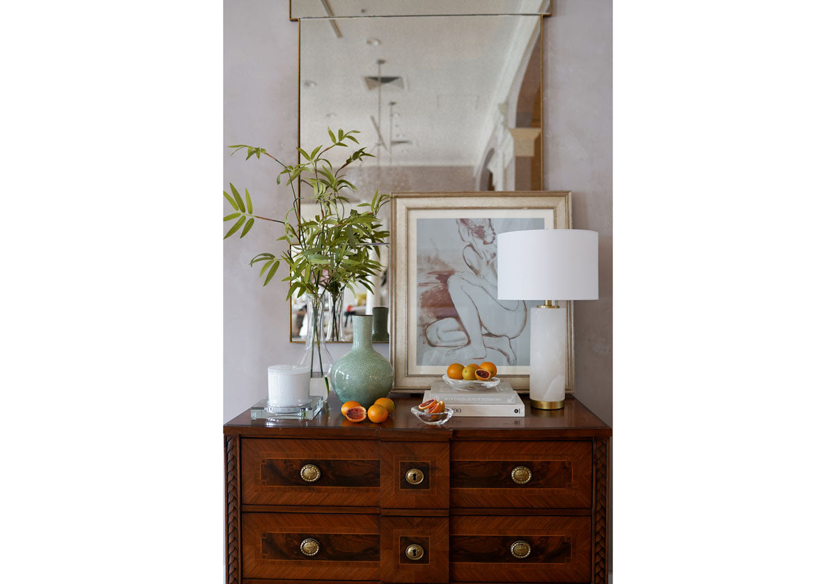 a dark brown dresser with a blue vase on top, an alabaster lamp, and a crystal candle dish. 