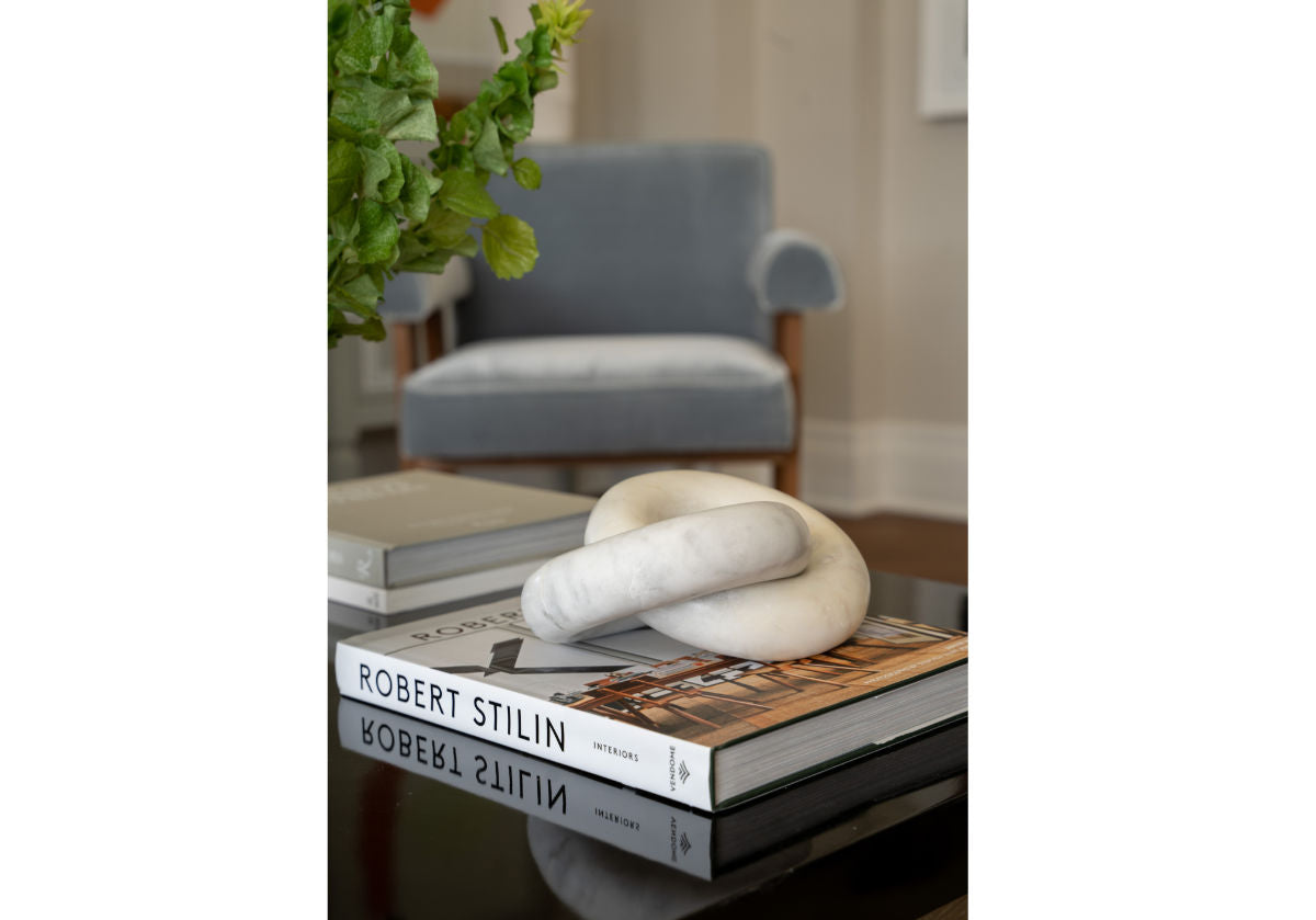 a lifestyle photo of a robert stilin book ona. coffee table with a white komo knot on top with a blue chair in the background. 