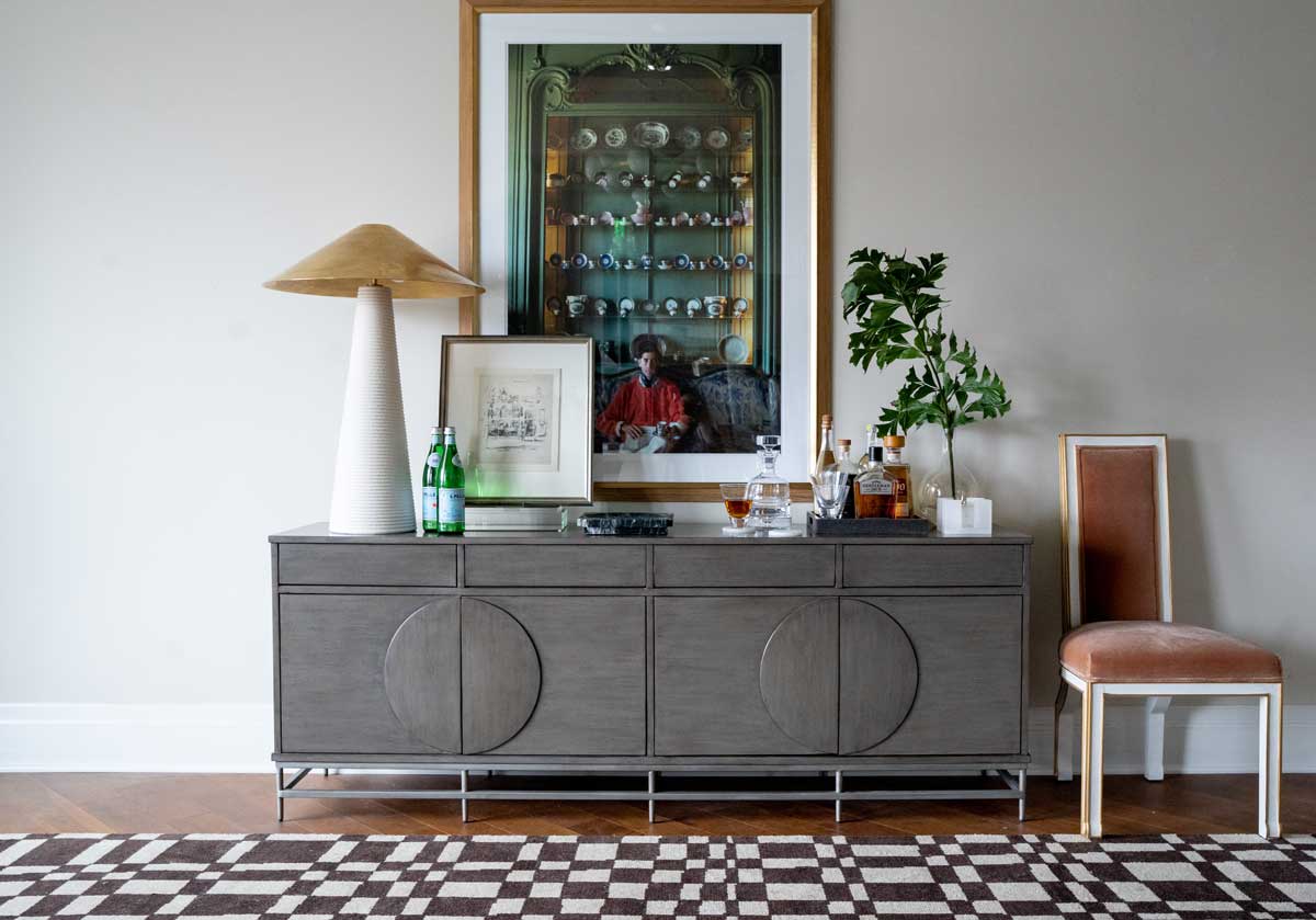 the felix chair is on the right side of a sideboard with a large white lamp on it and a decorative tray. 