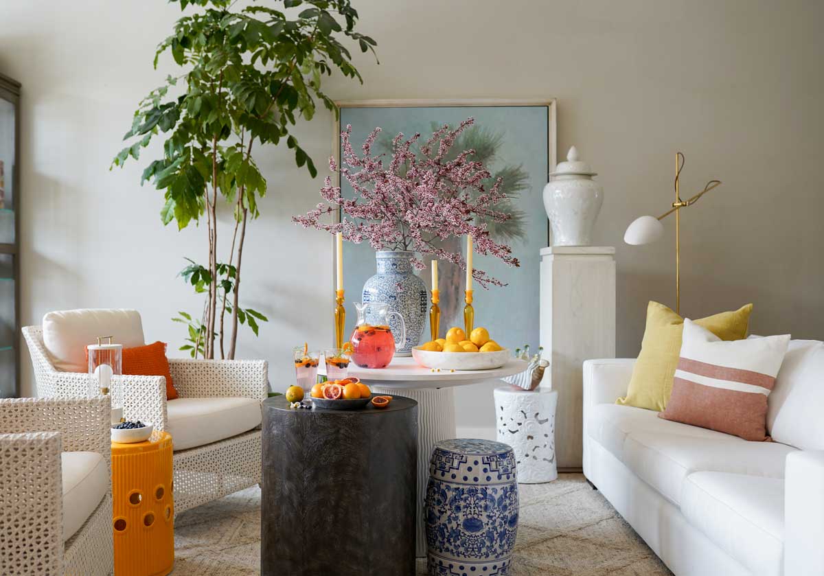 alice lane's charlotte garden stool can be seen in the back of the room on the floor next to a pedestal. there are 2 other garden stools in the picture, one orange and one blue and white. 