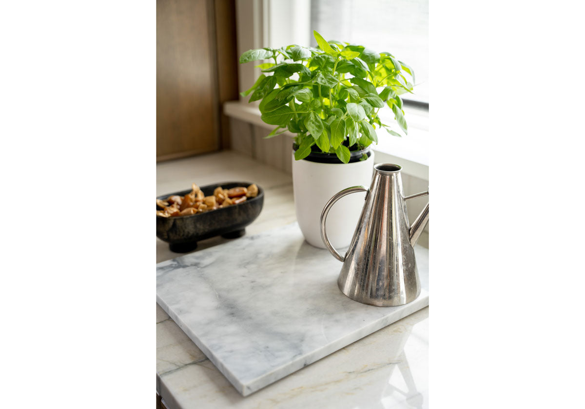 large, white marble cutting board featured with a plants and watering can on top of it. 